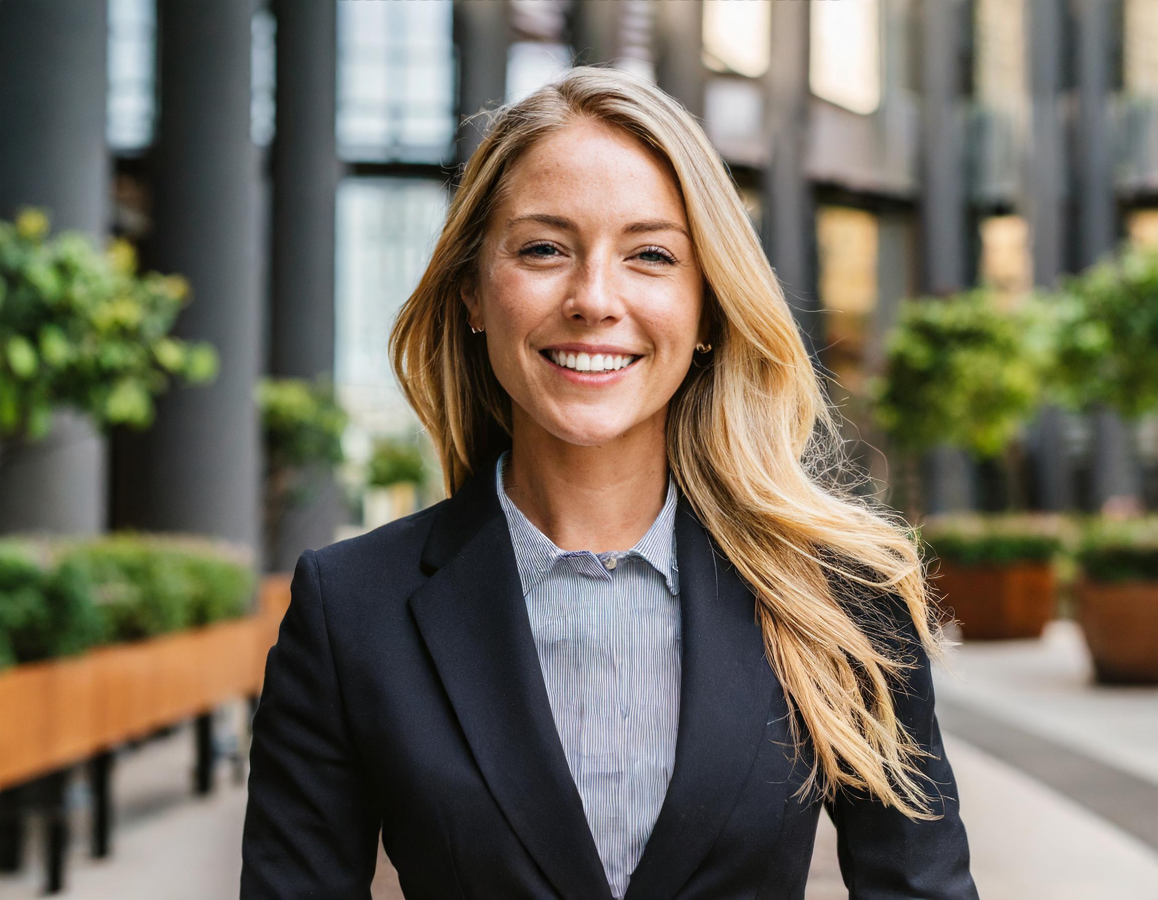 Frau mit dunklem Haar in einem professionellen Büro-Outfit, lächelnd